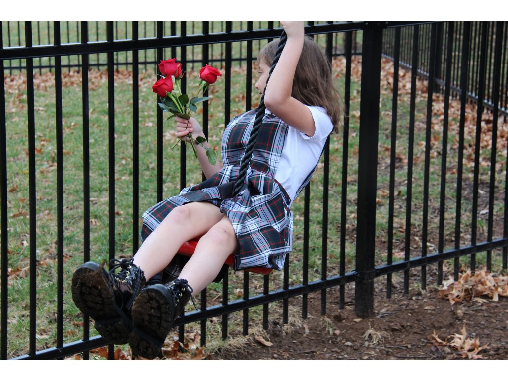 Young girl hanging on fence while holding roses