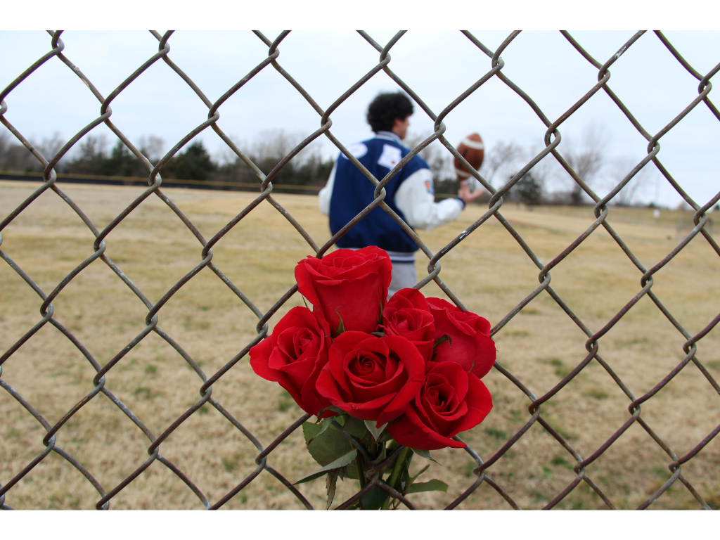 Boy holding football and chain fence with roses