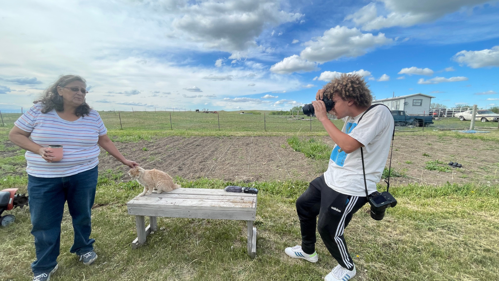 Student shooting a photograph of two individuals in front of a field.