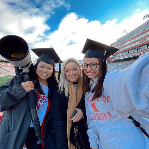 Three CoJMC graduates with camera at Memorial Stadium