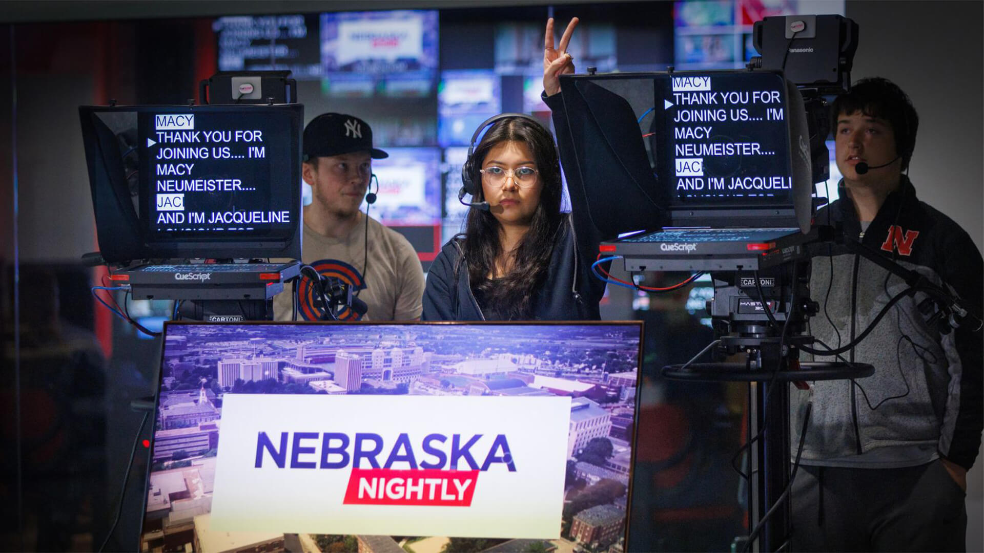 Student directors stand behind teleprompters and give hand signals