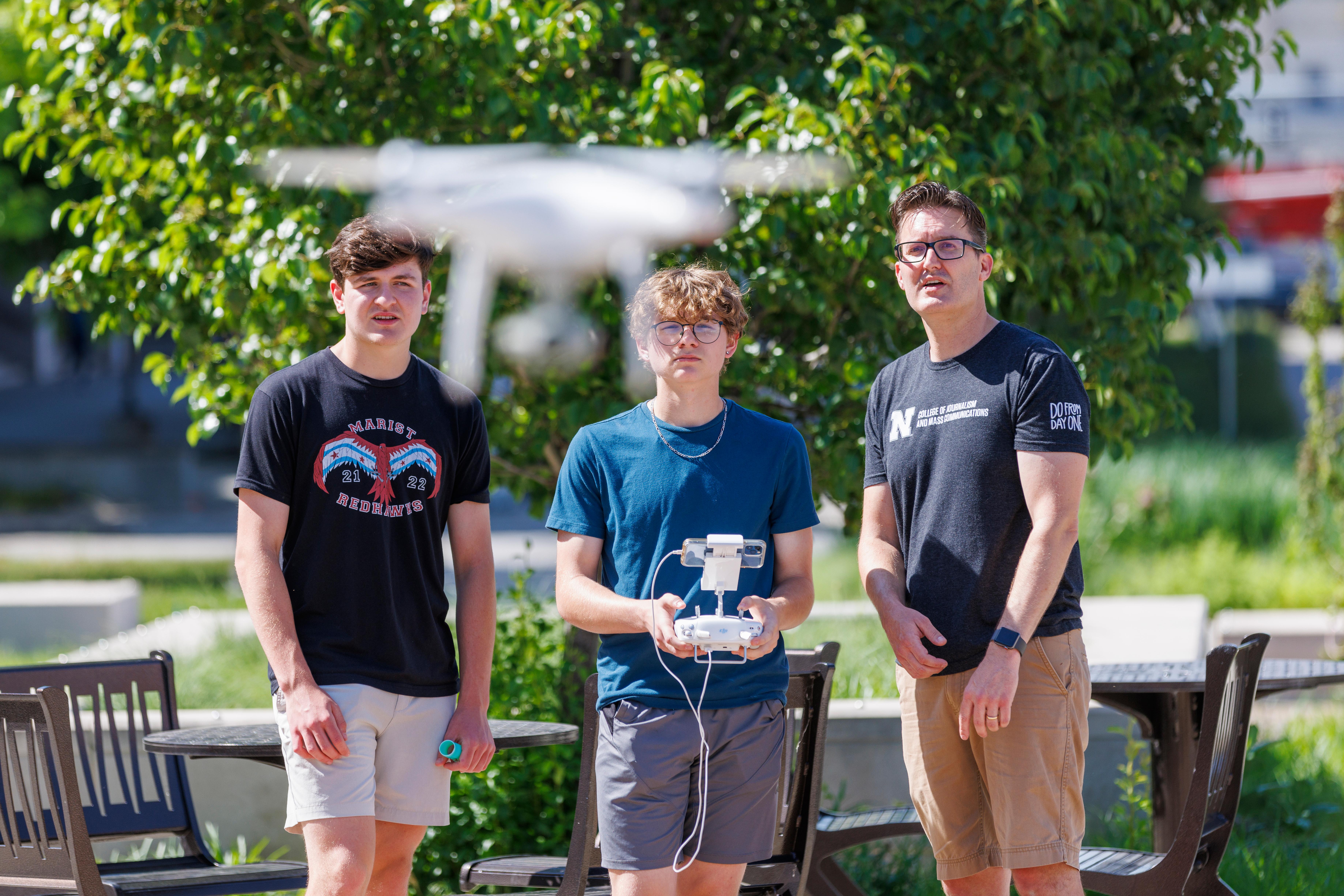 Three men stand and fly a drone