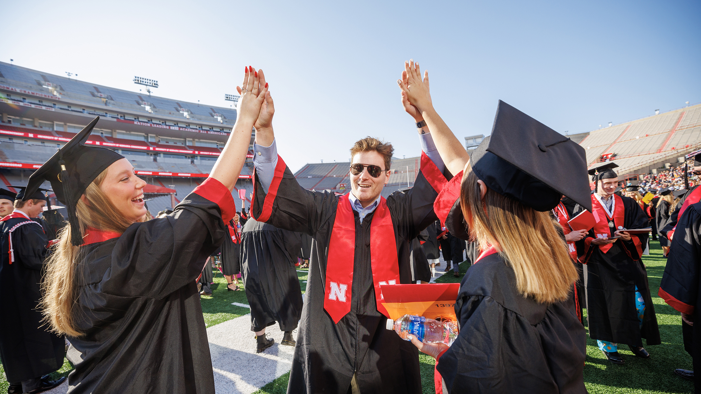 Three student high five wearing graduation caps and gowns