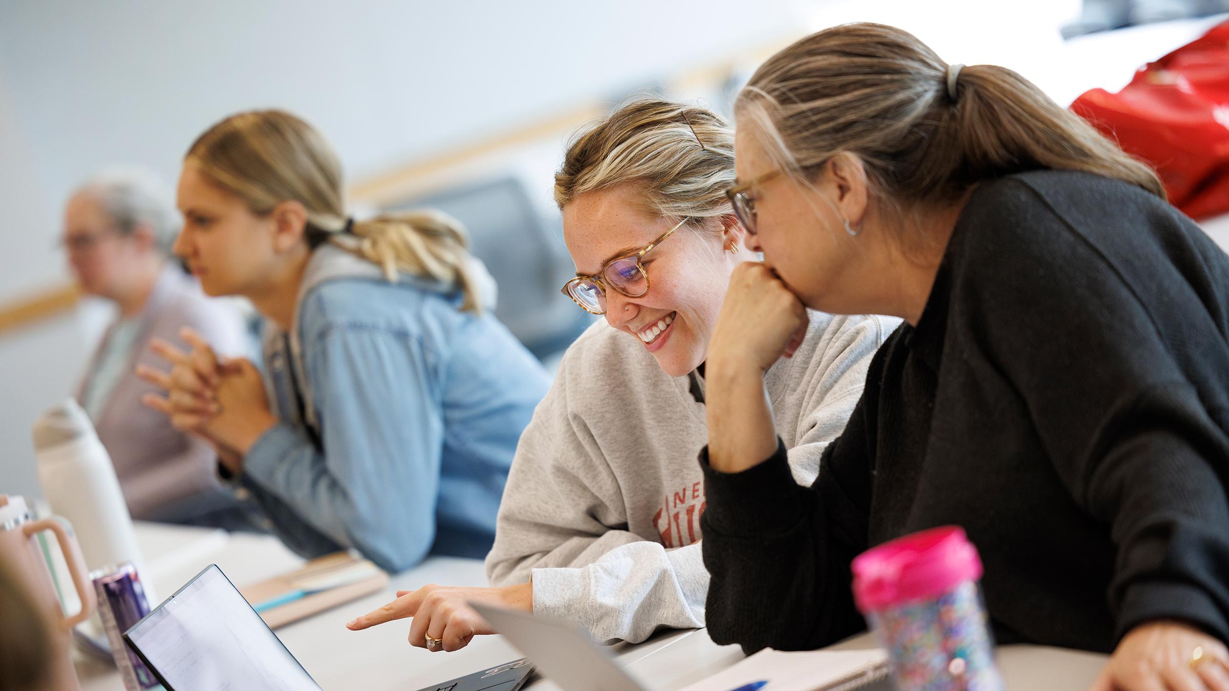 Two women sit at a desk lookng at a computer