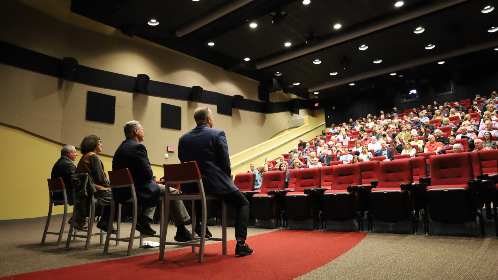 Four people sit on chairs in font of an auditorium