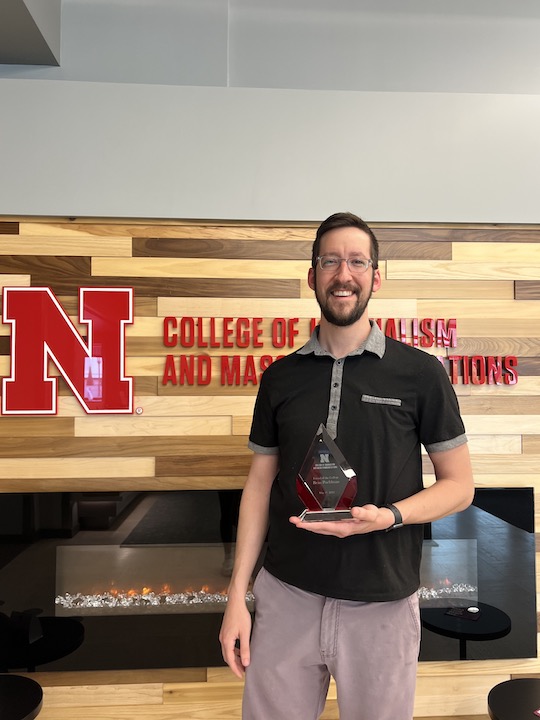 Friend of the College Award recipient Beau Poehlman, video production supervisor at Ameritas and volunteer professional-in-residence holds his award in the Andersen Hall lobby.