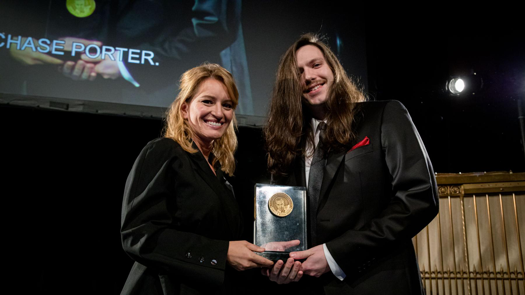 Two people stand holding an award