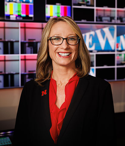 Dean Sheri Veil standing in front of TV screens in the CoJMC studio.