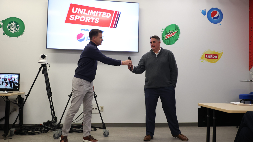 Pepsi Cola of Lincoln CEO Kirk Anderson hands the mic to Kevin Lambert, another Pepsi executive, during the Pepsi Unlimited Sports Lab Grand Opening.