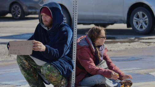 Payden Bain sits with Rebecca Mitchell on the traffic island near Hy-Vee in Lincoln, Neb., sharing a warm meal he received. As they sit together, they find comfort in each other's company.