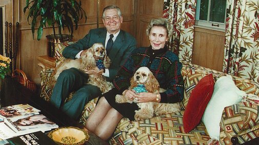 A man, a woman and two dogs sit on a couch