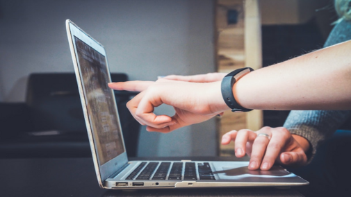 Laptop open on a desk with someone pointing at the screen