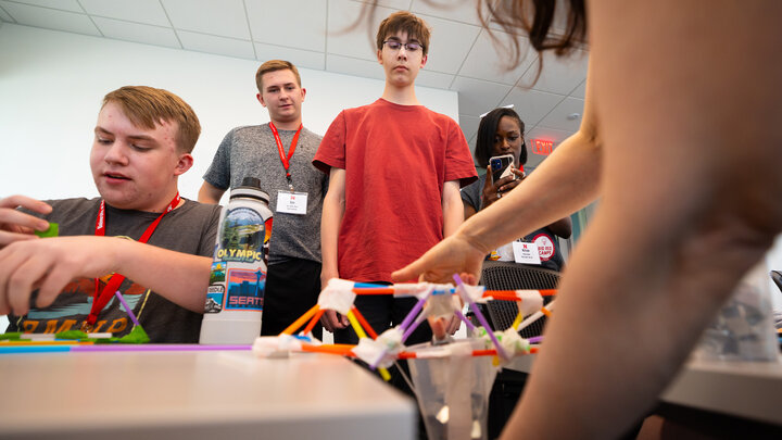oe Lake (red shirt) and Ryne Callahan watch as Rachel Rose, coordinator of engineering outreach, places heavy metal washers into a cup to see how much weight their straw-and-tape bridge can hold. The two, both high school juniors, participated in the engineering camp offered as one of Nebraska 4-H's Big Red Summer Academic Camps.