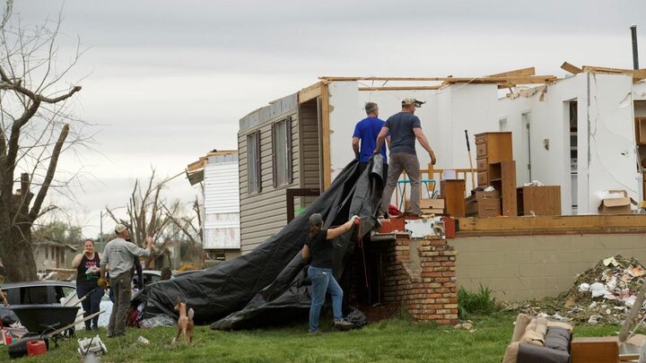 A group drags a tarp over what used to be the interior of an Omaha resident's home in the city's Elkhorn neighborhood on Saturday, April 27. The home, sitting on the corner of Appaloosa Drive and North 215th Circle, was one of many in the neighborhood without a roof and walls Saturday. Other homes in the area faced even more devastation, with the only remnants being a foundation and walls reduced to piles of wood. 