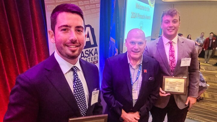 Three people stand holding awards