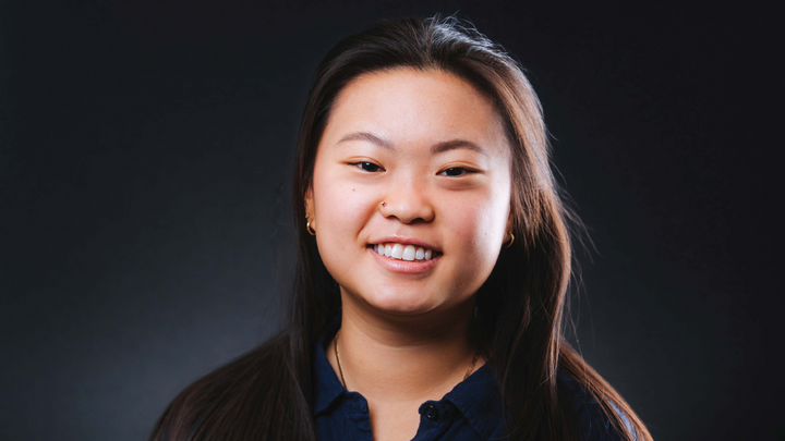 Dark-haired person in a dark shirt against a solid dark background.