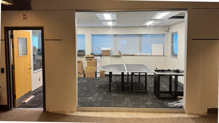 Room with a ping pong table, boxes, and equipment, viewed through a large glass window.