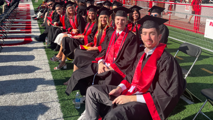 Students sit in a row in graduatin caps and gowns