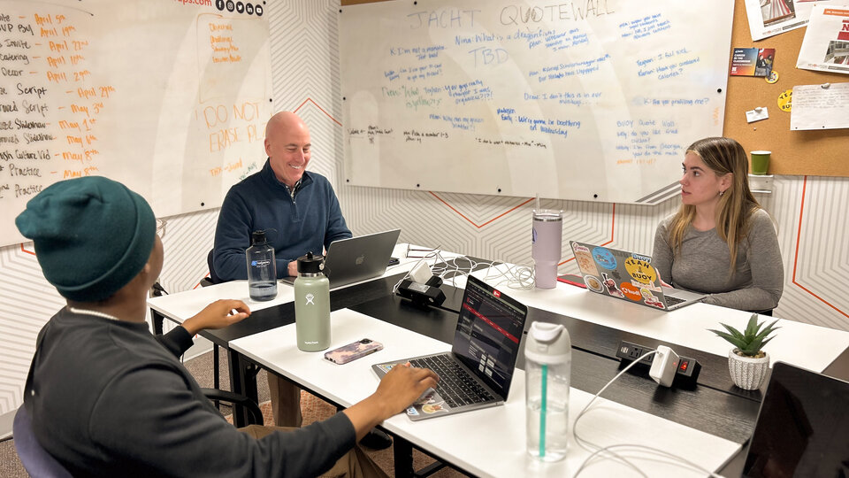 Three people sit around a table working on laptops