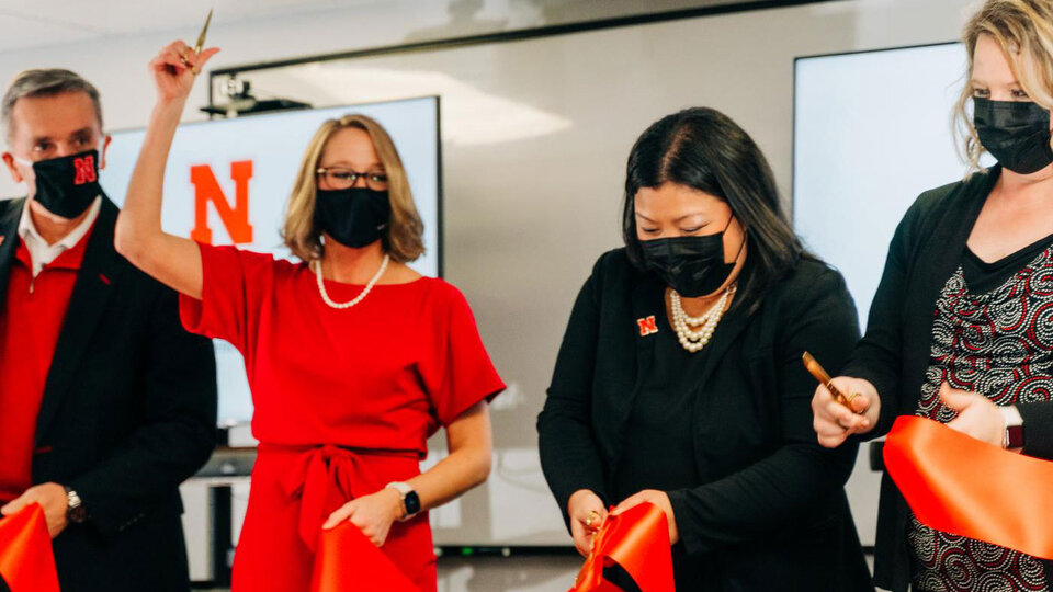 Four people cut a red ribbon with gold scissors