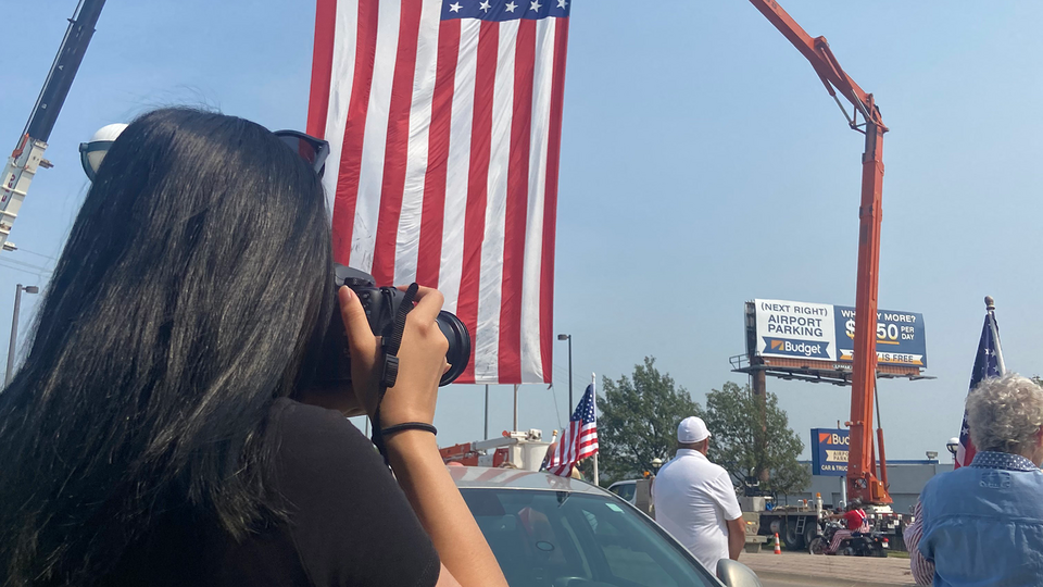 woman takes a photograph in front of an american flag 