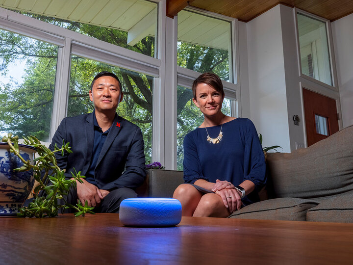 Two people sit on a couch looking at a digital voice assistant