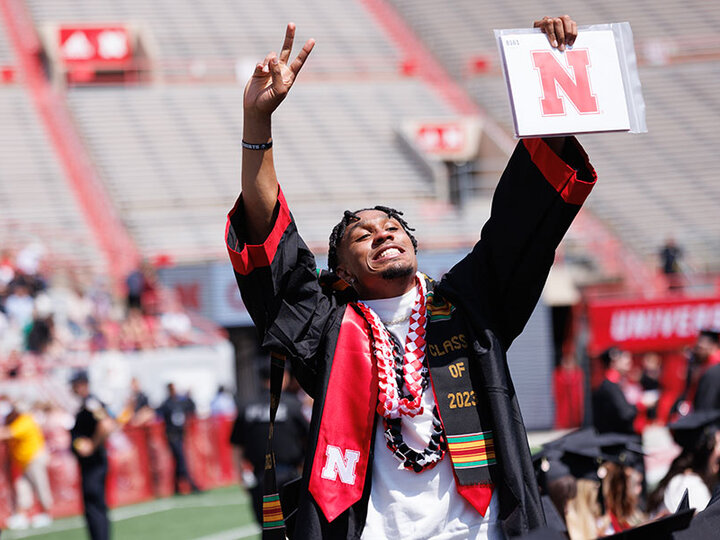 Man in graduation garb holding up his hands