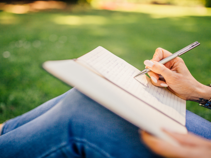 person sitting on the ground writign in a notebook