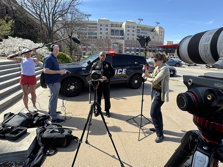 People stand in front of a setup of video cameras in front of Memorial Stadium.