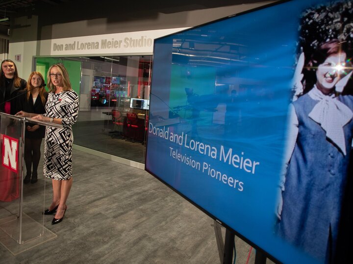 Woman speaks from a podium next to a TV screen