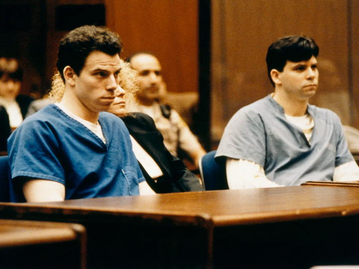 Two men sit at a table in a court room. 