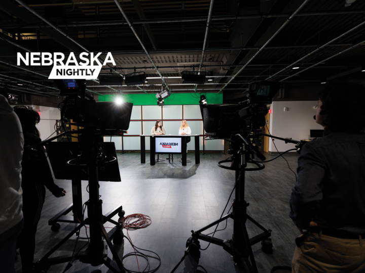 Two students sit at an anchor desk in a news studio