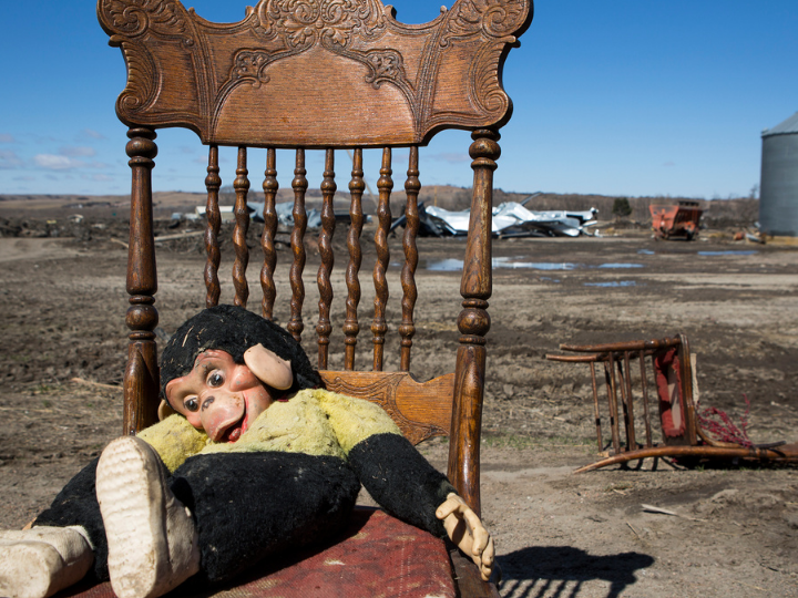 dirty toy monkey sits on a wooden chair in front of a flooded field