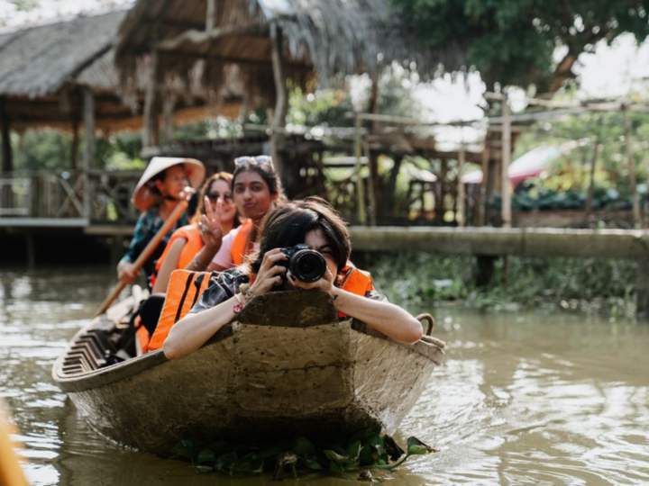 students sitting on a boat while one takes a picture from her camera