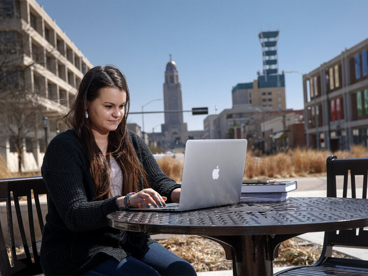 women works on a latop outside with buildings in the background