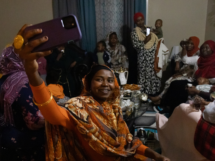 In this photo from Marissa Lindemann's essay "Sister Get-Together," Aisha Ibrahim holds up her phone to take a selfie with a group of Sudanese women and children Feb. 22 in her Lincoln apartment. The women have found a sense of community in the group, which was formed after many of them met while visiting a friend after she had a baby in 2021. In Sudanese culture, 40 days after a woman has given birth, the women of the community visit to celebrate.