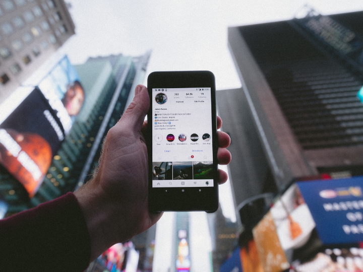 hand holding cell phone in front of tall buildings