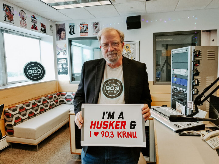 Man holds a sign that reads "I'm a Husker & I love 90.3 KRNU"