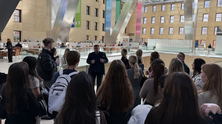 Group of students listen to a speaker in a building lobby