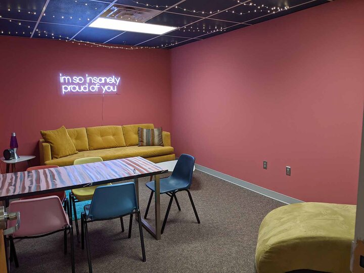 Office with pink walls, a yellow couch and a neon sign that reads "I'm so insanely proud of you"