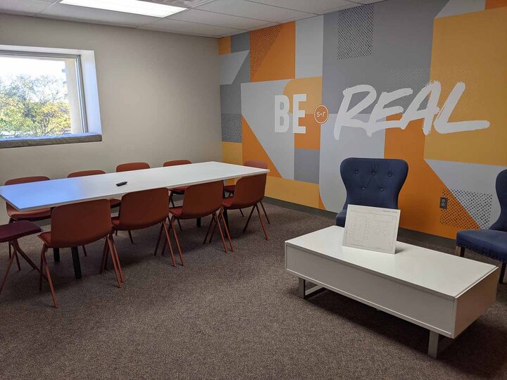 Conference room with blue and orange chairs and a patterned wall that reads "Be Real"