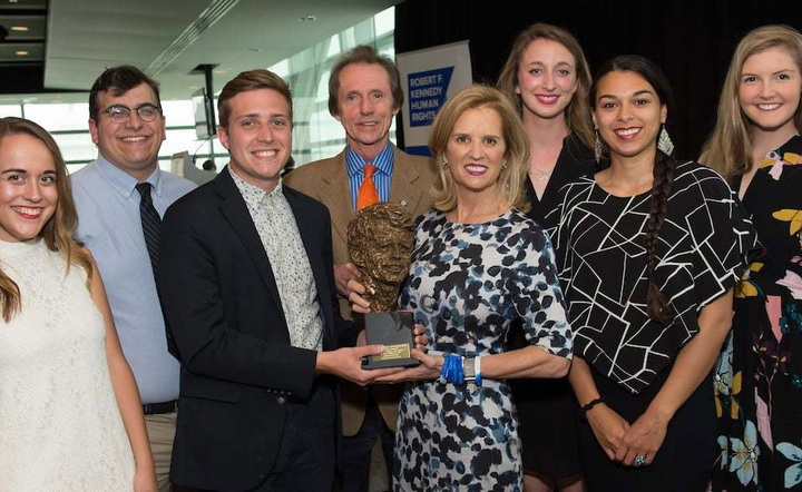 Eight people stand holding an award